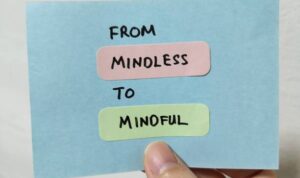 Hand holding a note showing the words From Mindless To Mindful